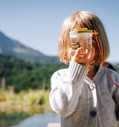 Kind hält sich Glas mit Fund aus dem Biotop vor das Gesicht