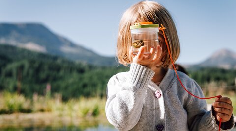 Kind hält sich Glas mit einem Tier aus dem Biotop vor das Gesicht